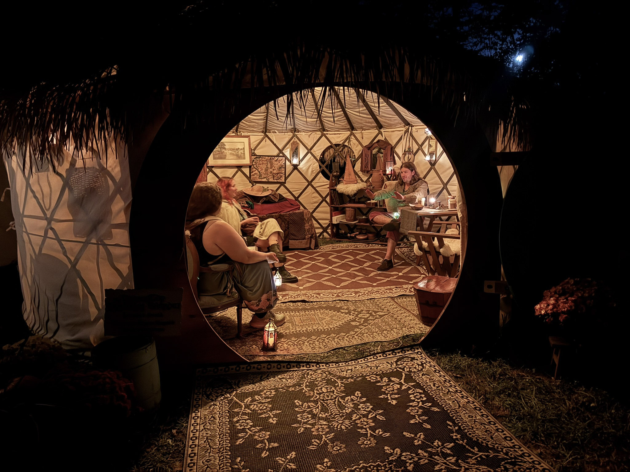 Looking through the open round door of a ThatchTop Burrow at night into a warm, lantern-lit interior