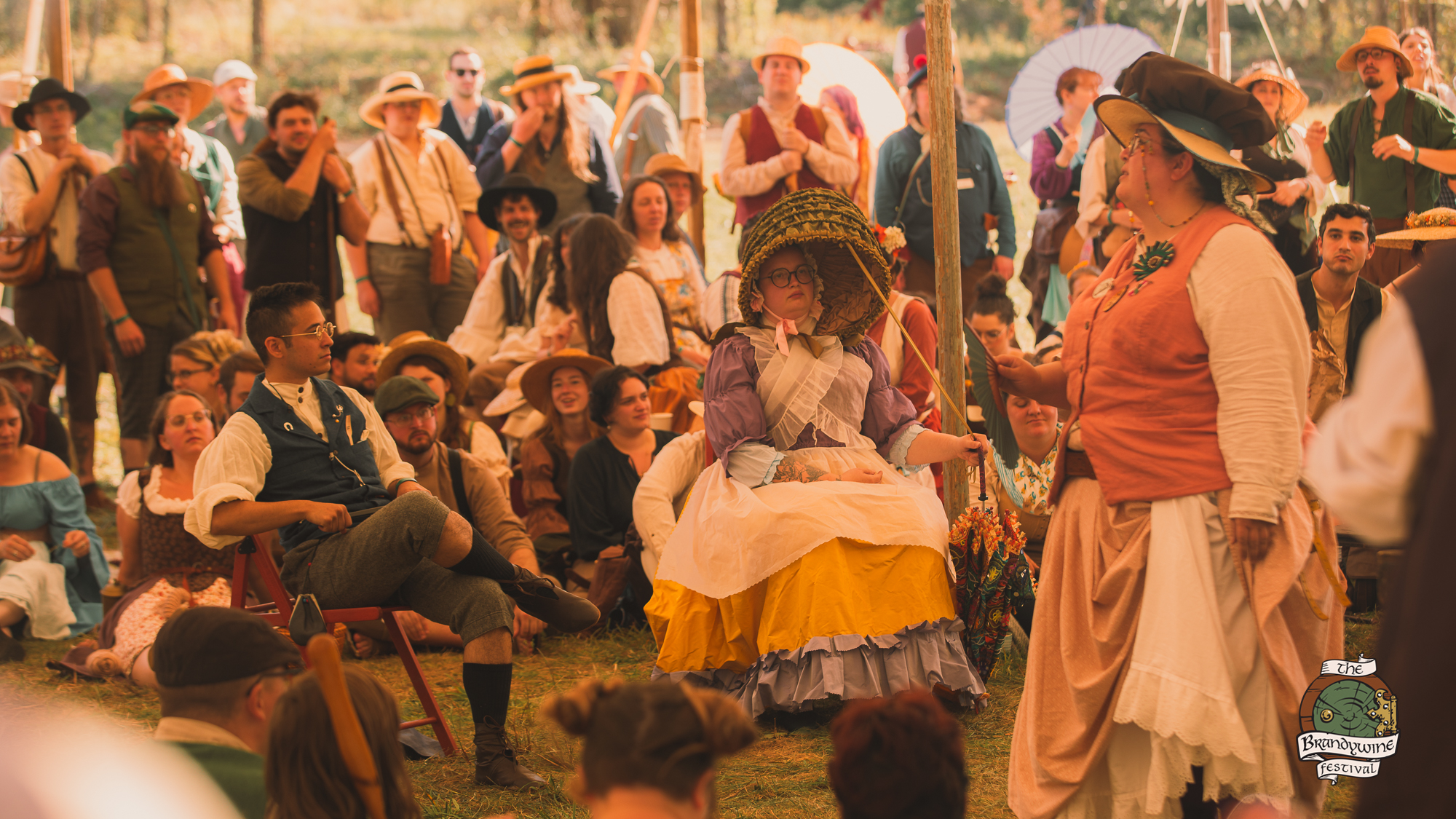 A costumed performer addressing a gathered crowd in the festival square