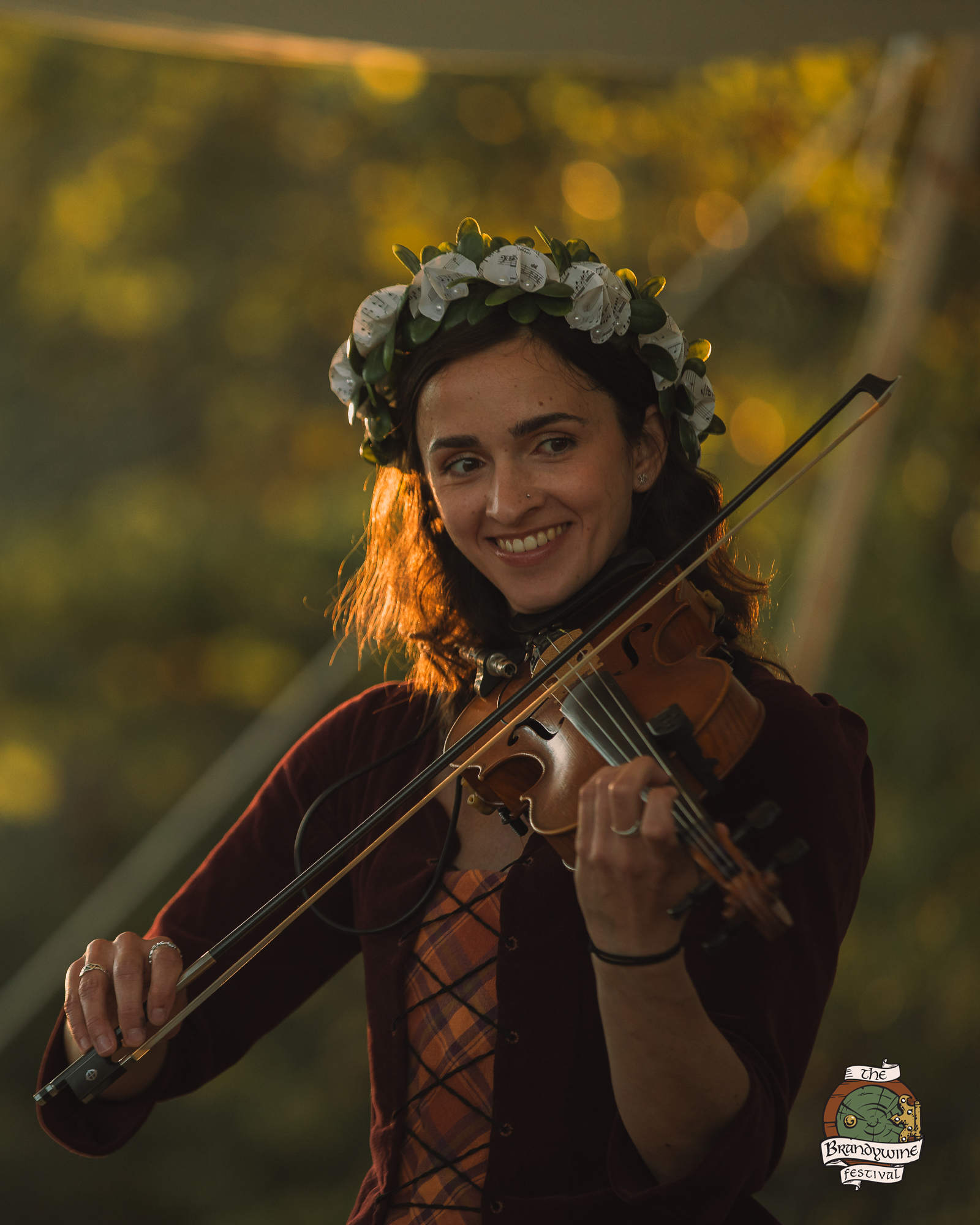 A smiling fiddle player in a flower crown at golden hour